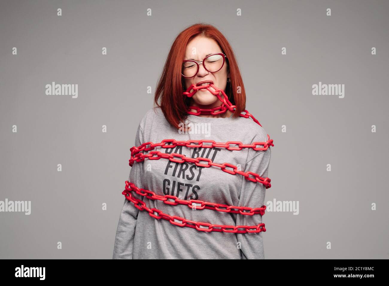 girl entangled in a chain,A red-haired woman with brown hair tries to get rid of the chain Stock Photo
