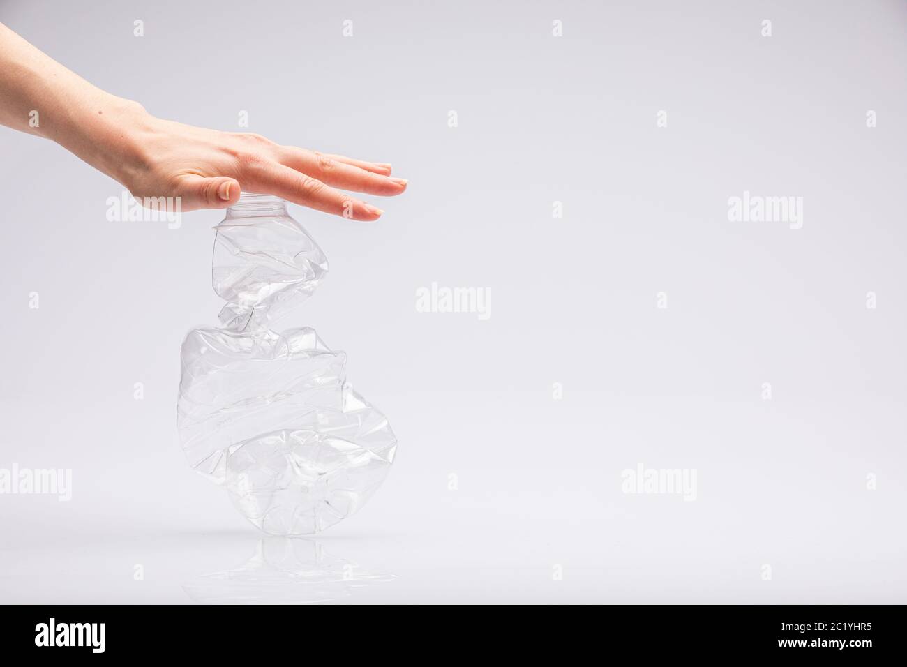 Closeup of a white people's hand crushing a crumpled plastic bottle in front of a white