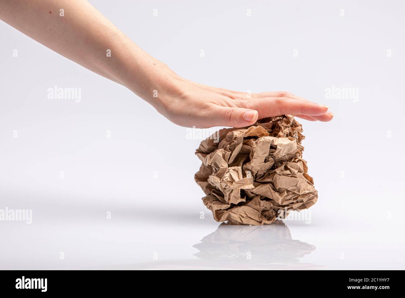 Closeup of a white people's hand crushing a crumpled piece of brown