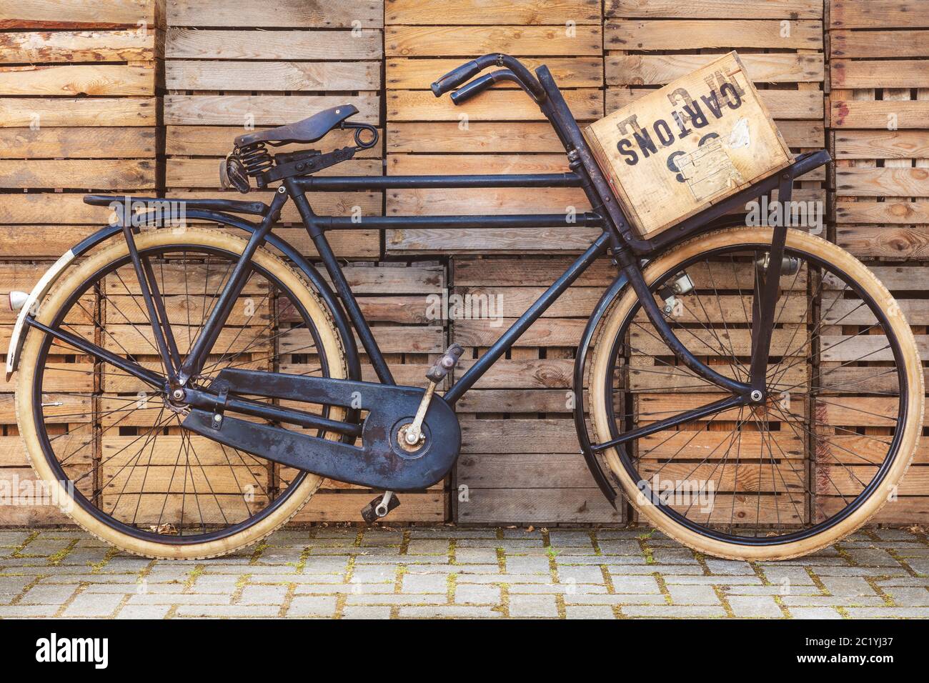 Vintage black cargo transport bicycle with crate carrier in front of old wooden crates Stock Photo