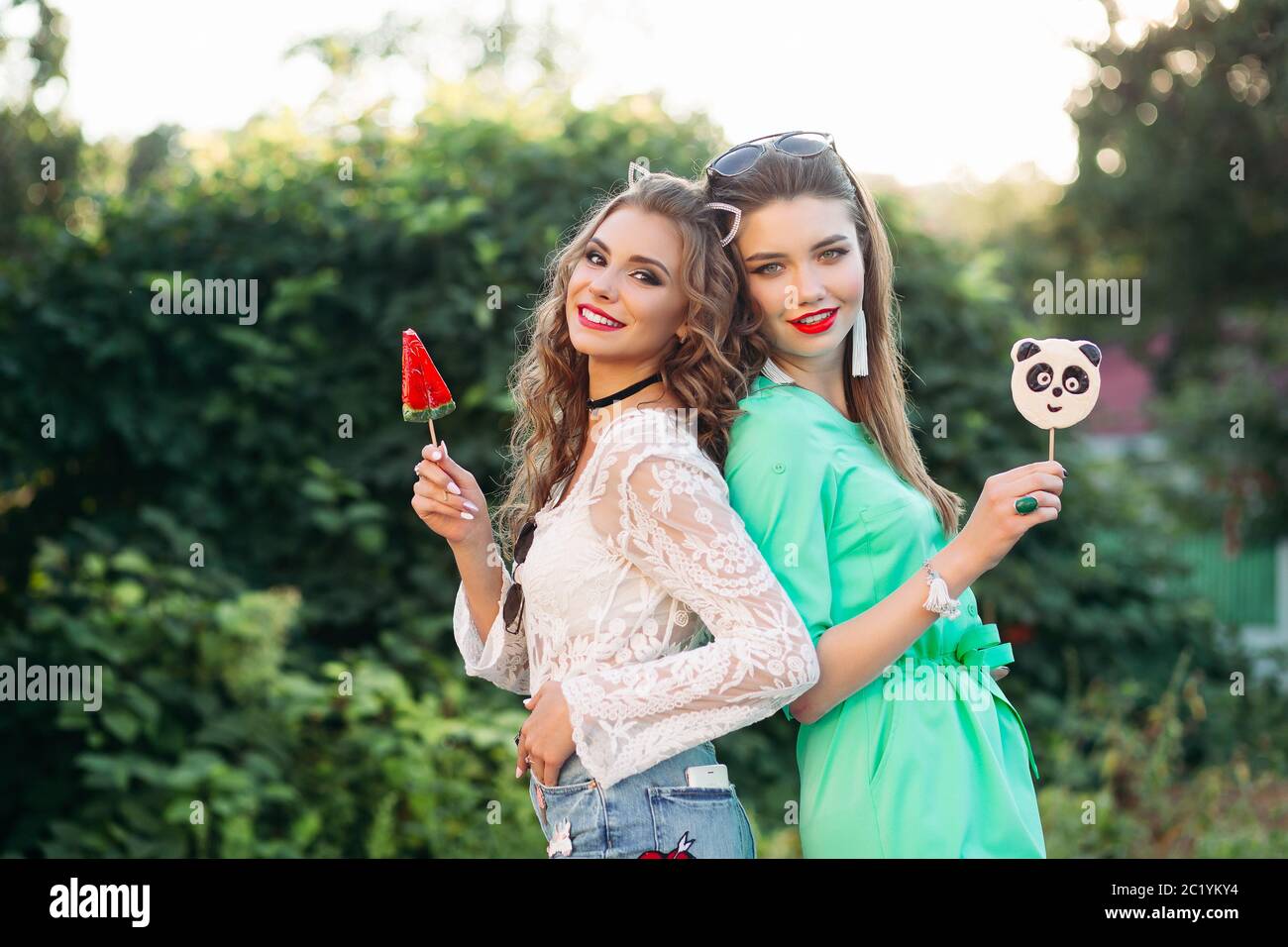 Two pretty and fashionable girlfriends holding candies on stick. Stock Photo