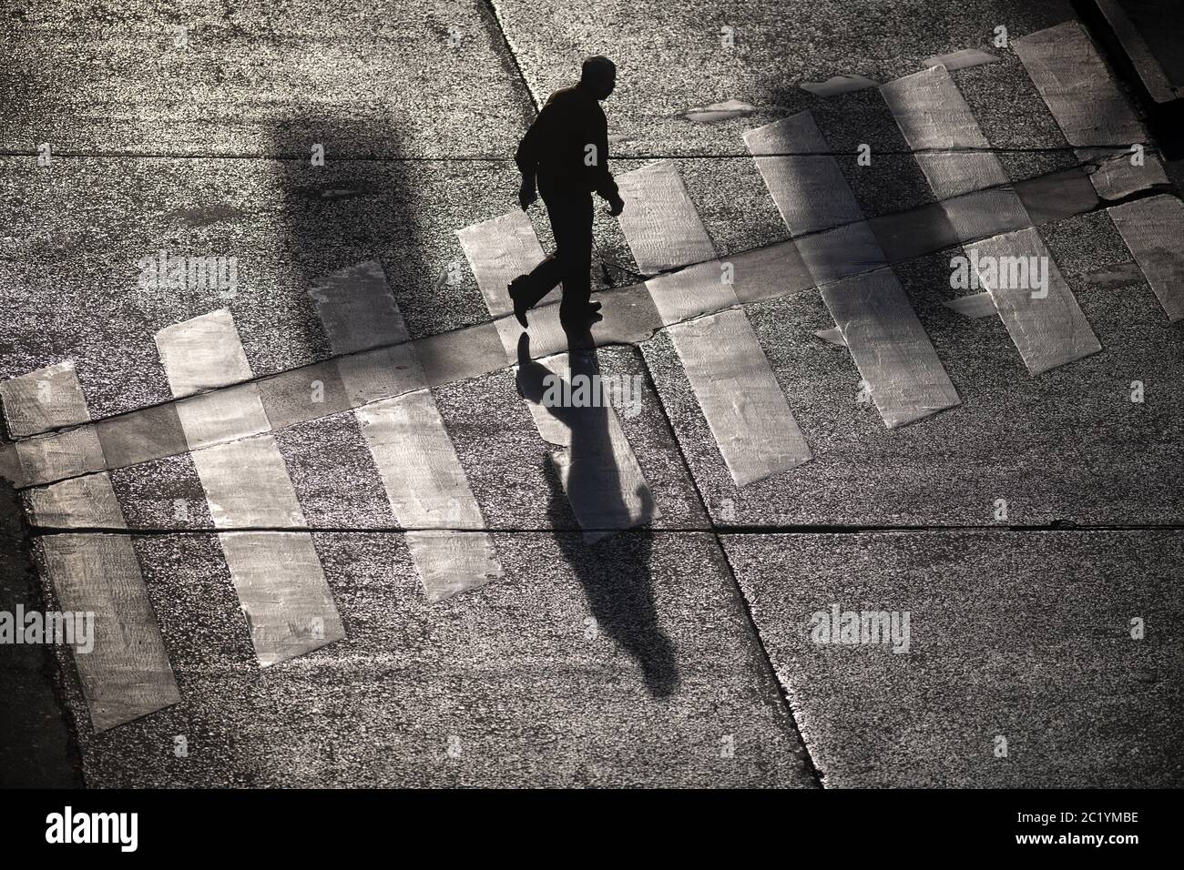 Top view of a silhouetted man and his shadow crossing the crosswalk Stock Photo