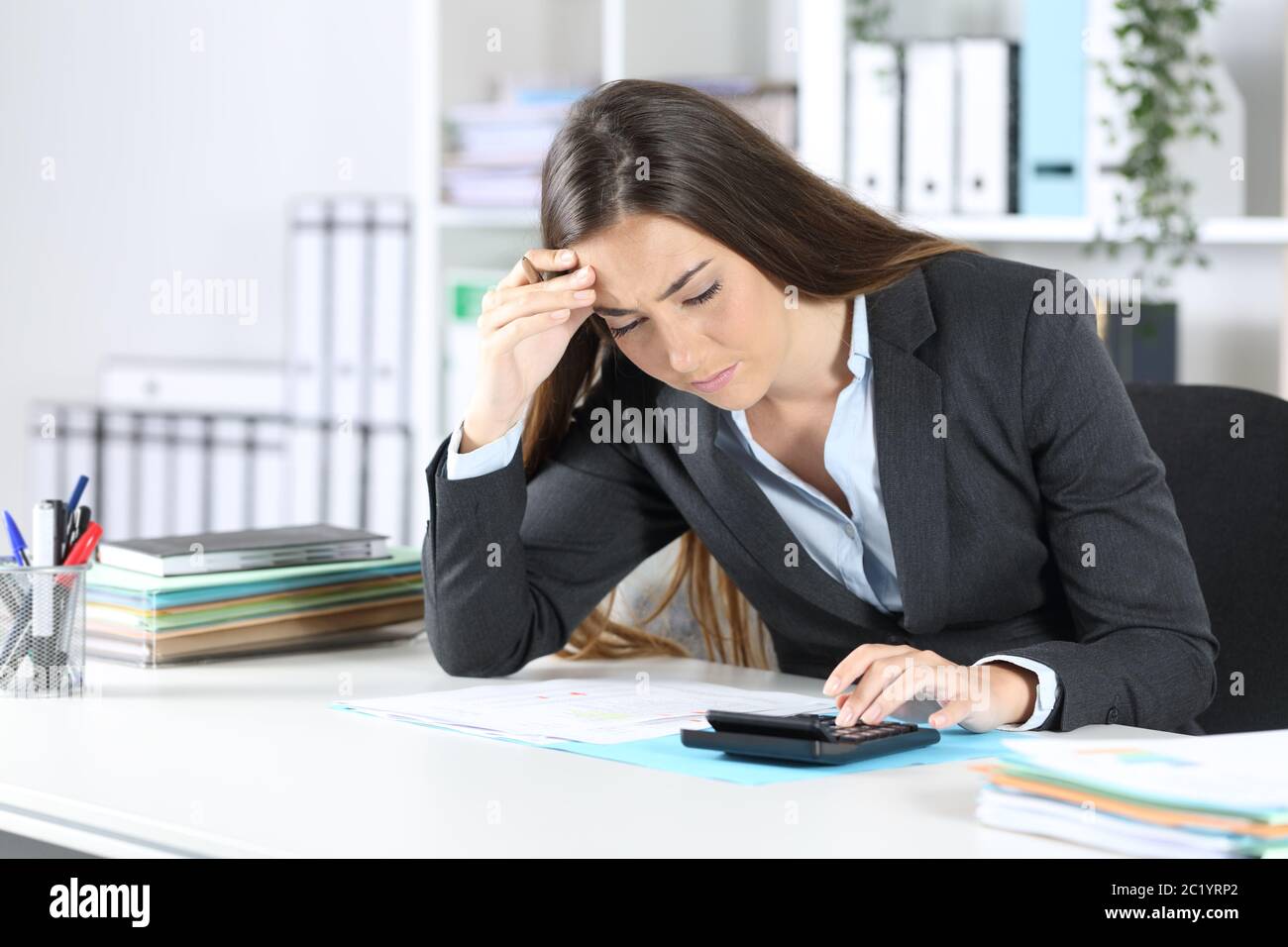Worried bookkeeper woman checking calculator result sitting on a desk at office Stock Photo