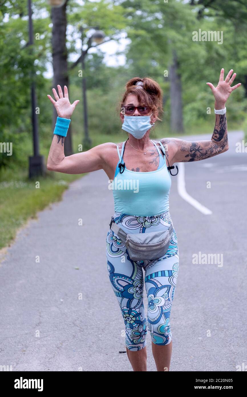 An attractive middle aged woman running on  the path near the Bayside Marina while wearing a mask over her mouth. In Bayside, Queens, New York.wears, Stock Photo