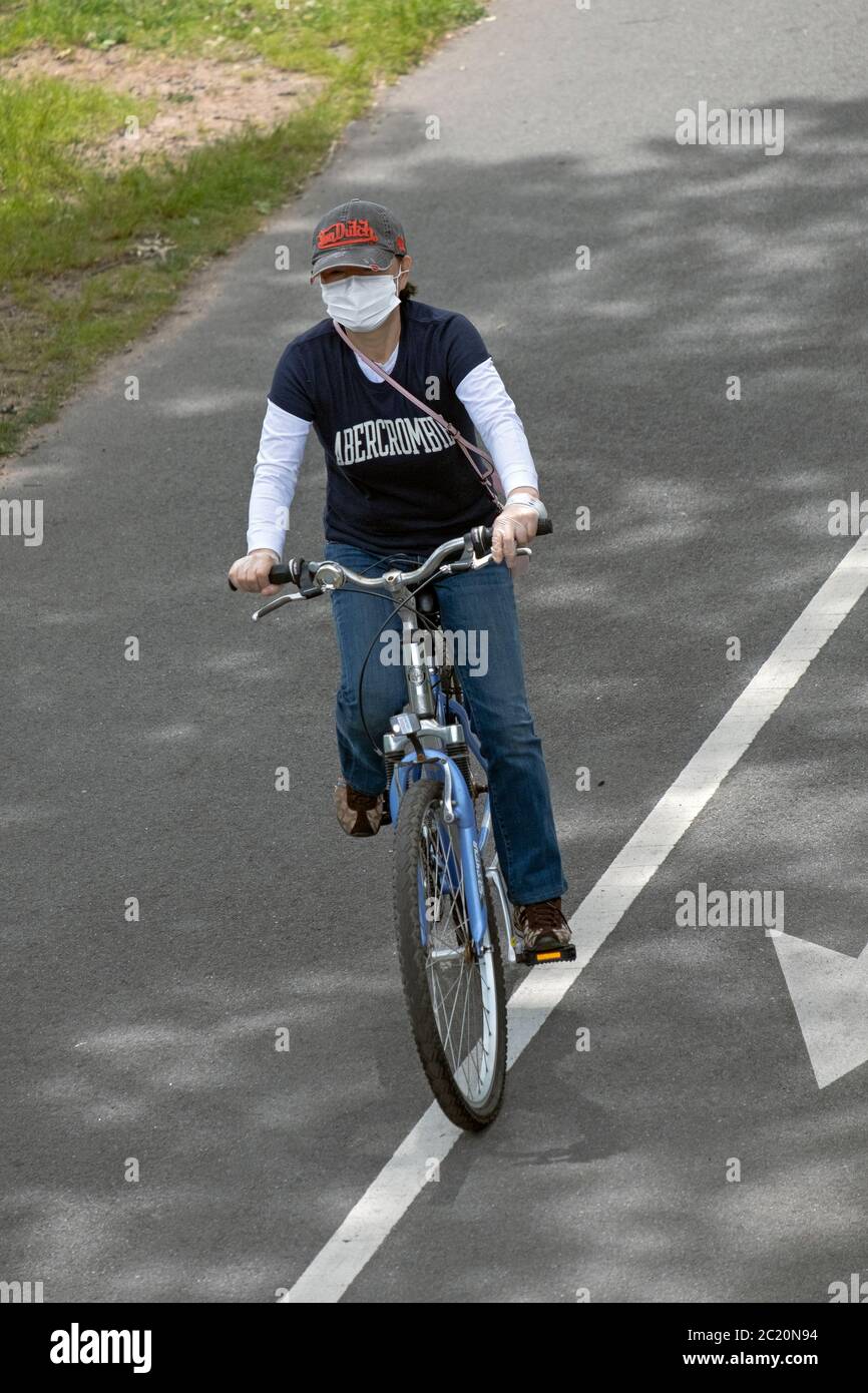 A young lady cycling while wearing a surgical mask and protective gloves. On a bike path near the Bayside Marina in Queens, New York. Stock Photo