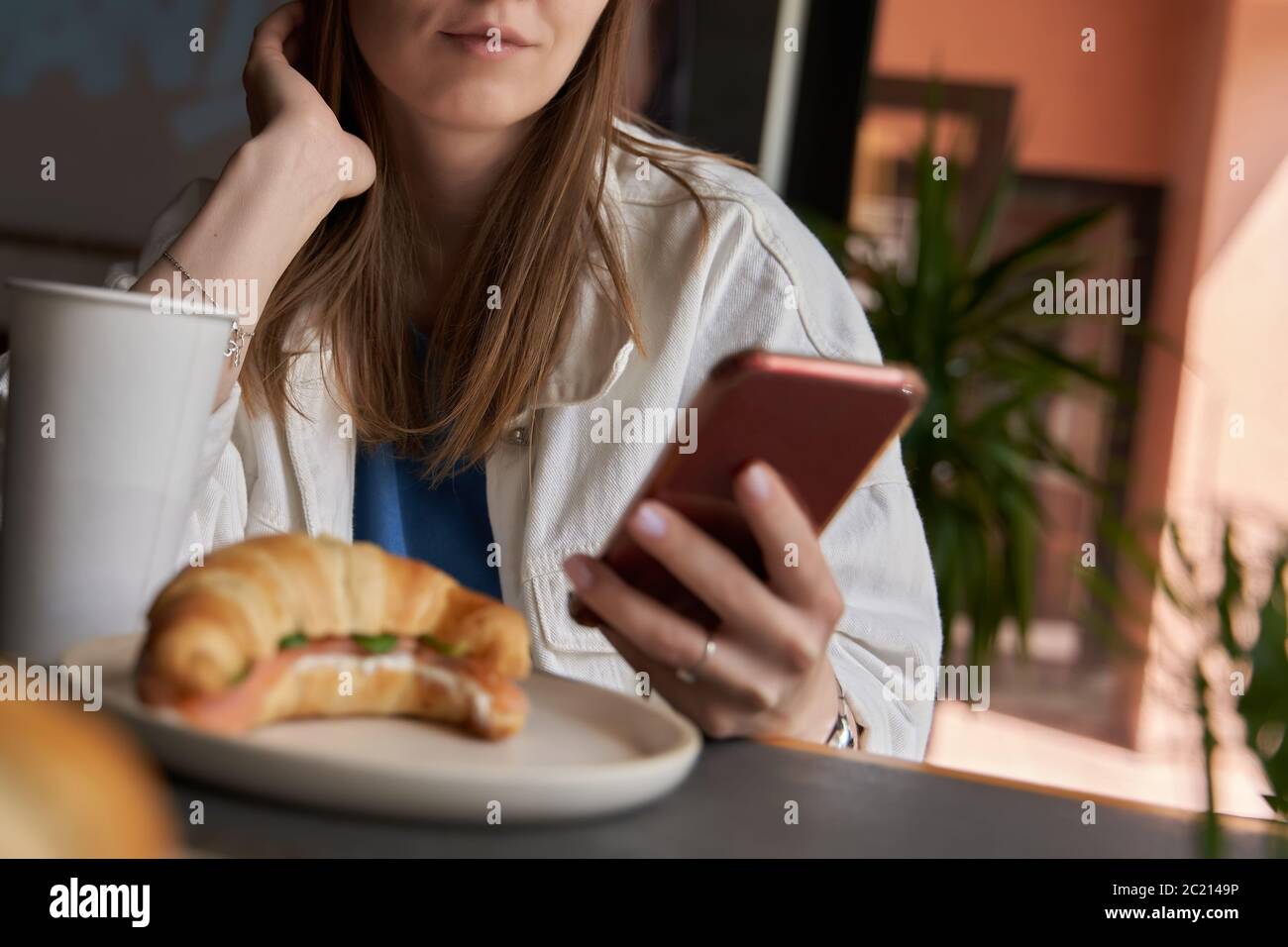 Woman typing text message on smart phone in a cafe. Cropped image of young woman sitting at a table with a coffee using mobile phone. Selective focus. Stock Photo