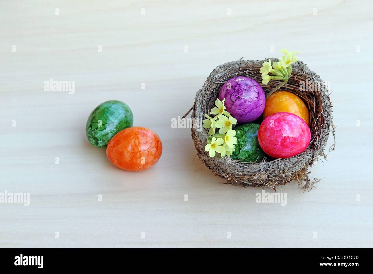 An Easter nest with colourful Easter eggs and primroses on a wooden background Stock Photo