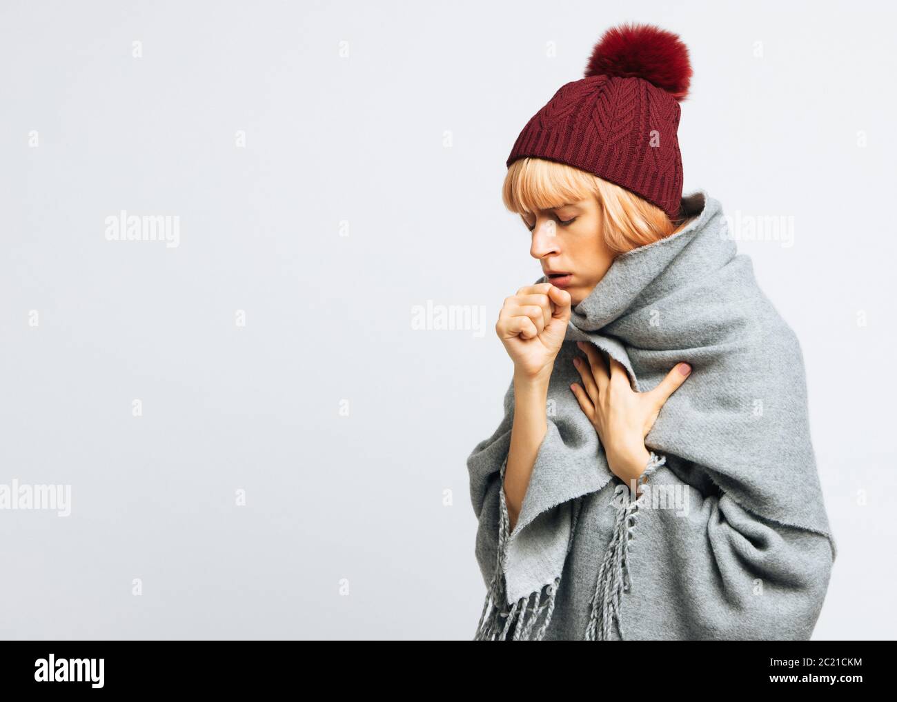 Cute sick young teen woman in red hat, wrapped in warm scarf coughing
