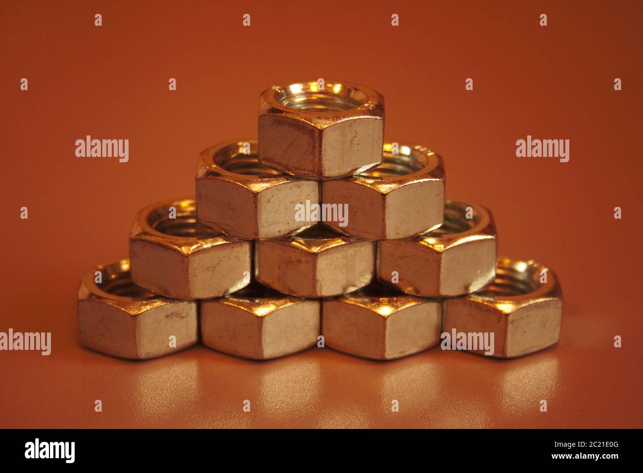 Pyramid from steel nuts on an orange-brown background. Stock Photo