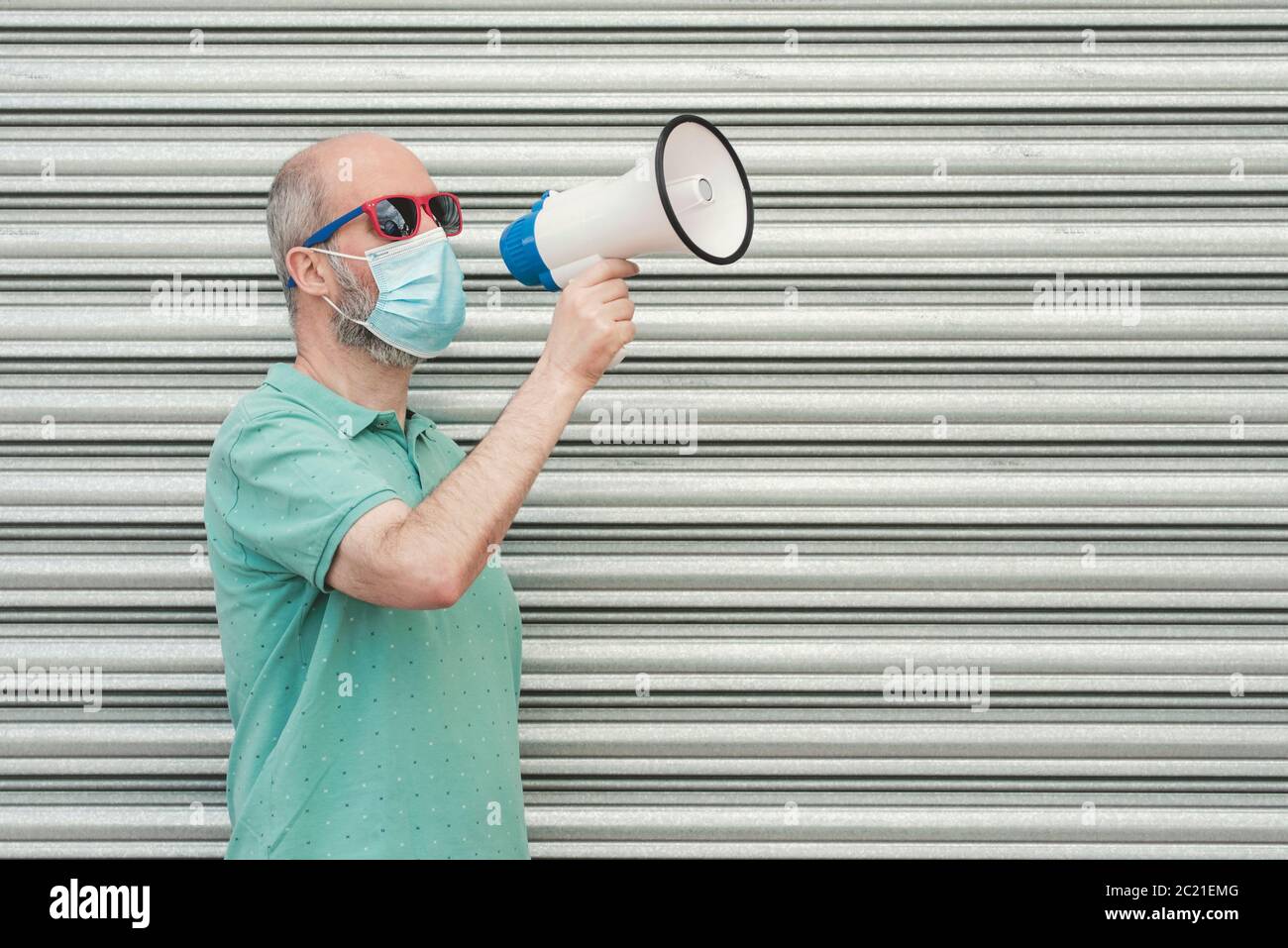 man with medical mask screaming with megaphone outdoor Stock Photo