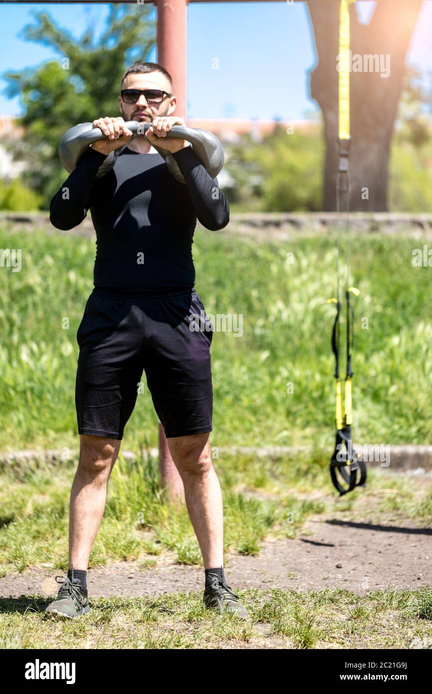 Strong young man exercising shoulders with kettle bell weights. Man Exercises with kettlebell in sunny weather. Stock Photo