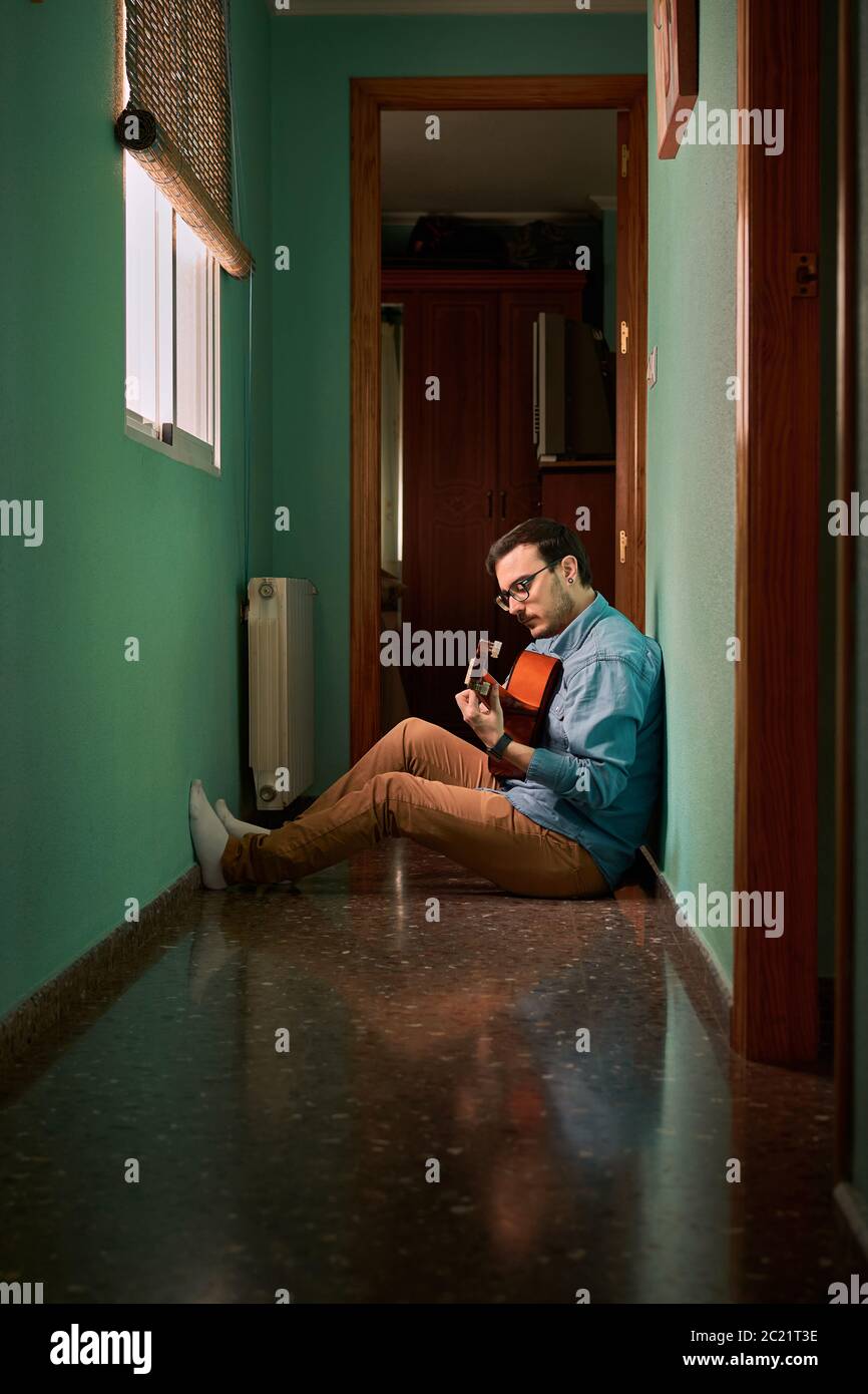 Young man plays guitar sitting in the hallway of his house Stock Photo