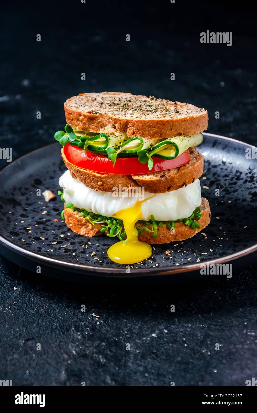Homemade Healthy Sandwich with Wholegrain Bread, Poached Egg Liquid Yolk, Cucumber, Tomato and Micro Herbs Watercress Salad on Plate Stock Photo