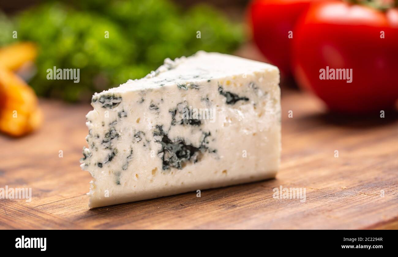 Slice of blue cheese on a cutting board with vegetables in the background Stock Photo