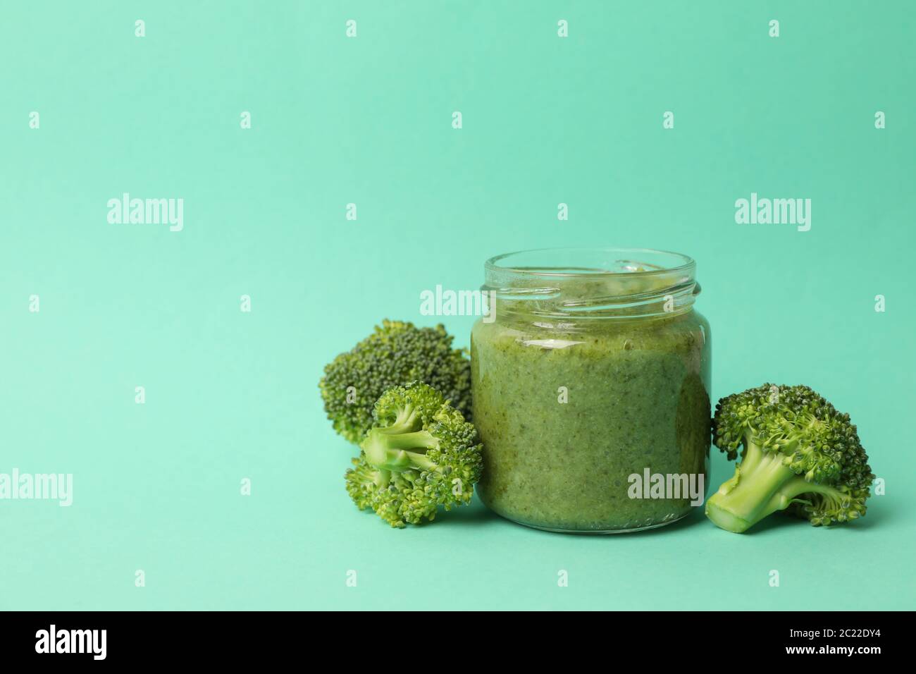 Glass jar with broccoli puree on mint background Stock Photo