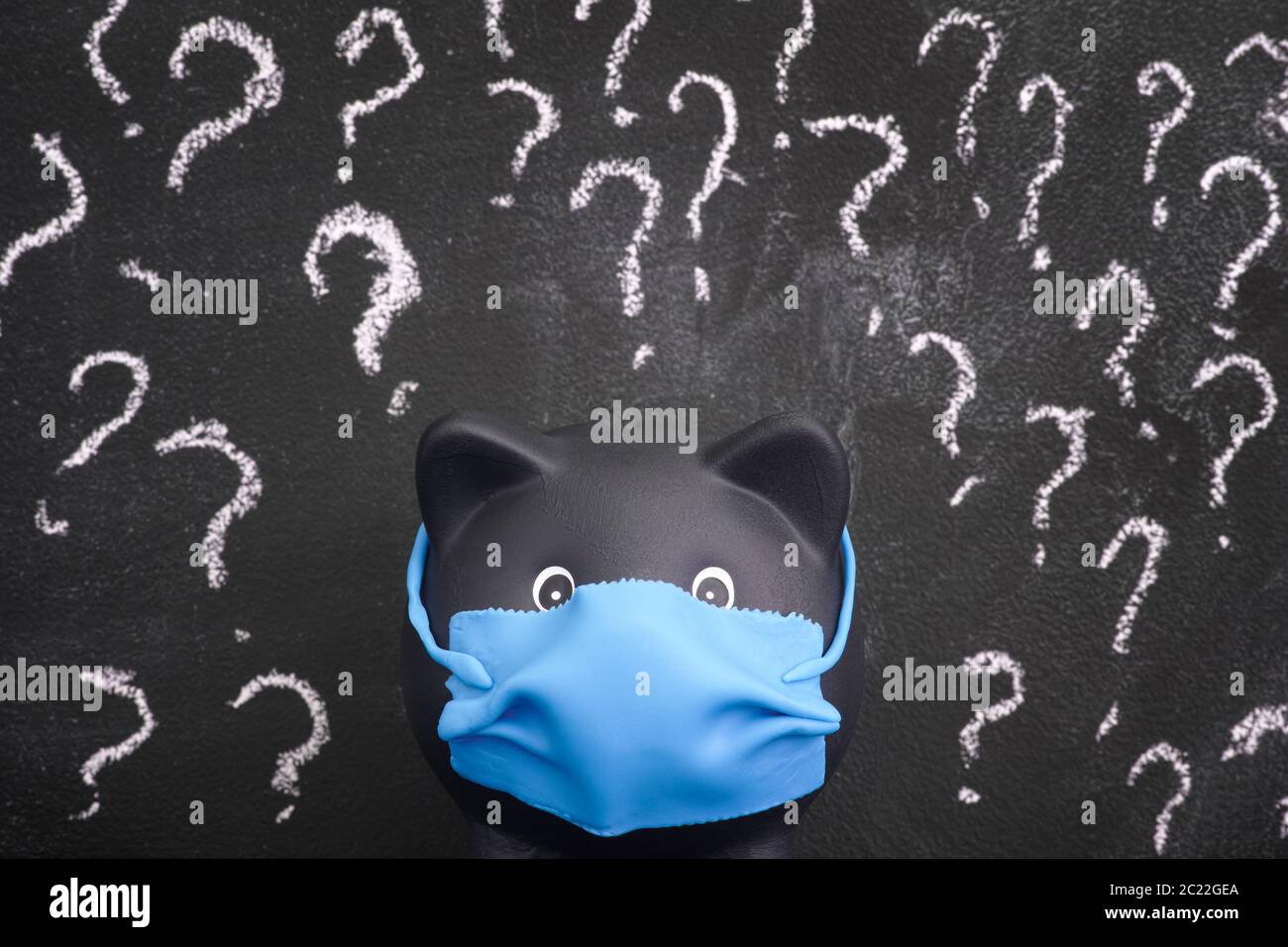 Black piggy bank wearing a face mask and standing against a blackboard with question marks on it. Close up. Stock Photo