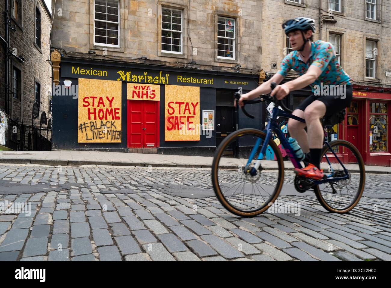 Edinburgh, Scotland, UK. 16 June, 2020. As shops open in England, Scottish shops and businesses remain closed, Streets are empty and pubs and shops are still closed with many boarded up. Bars might be allowed to open outside areas at end of week but currently they are only-permitted  to serve drinks to takeaway. Pictured; Cyclist rides past boarded up restaurant on Victoria Street.   Iain Masterton/Alamy Live News Stock Photo