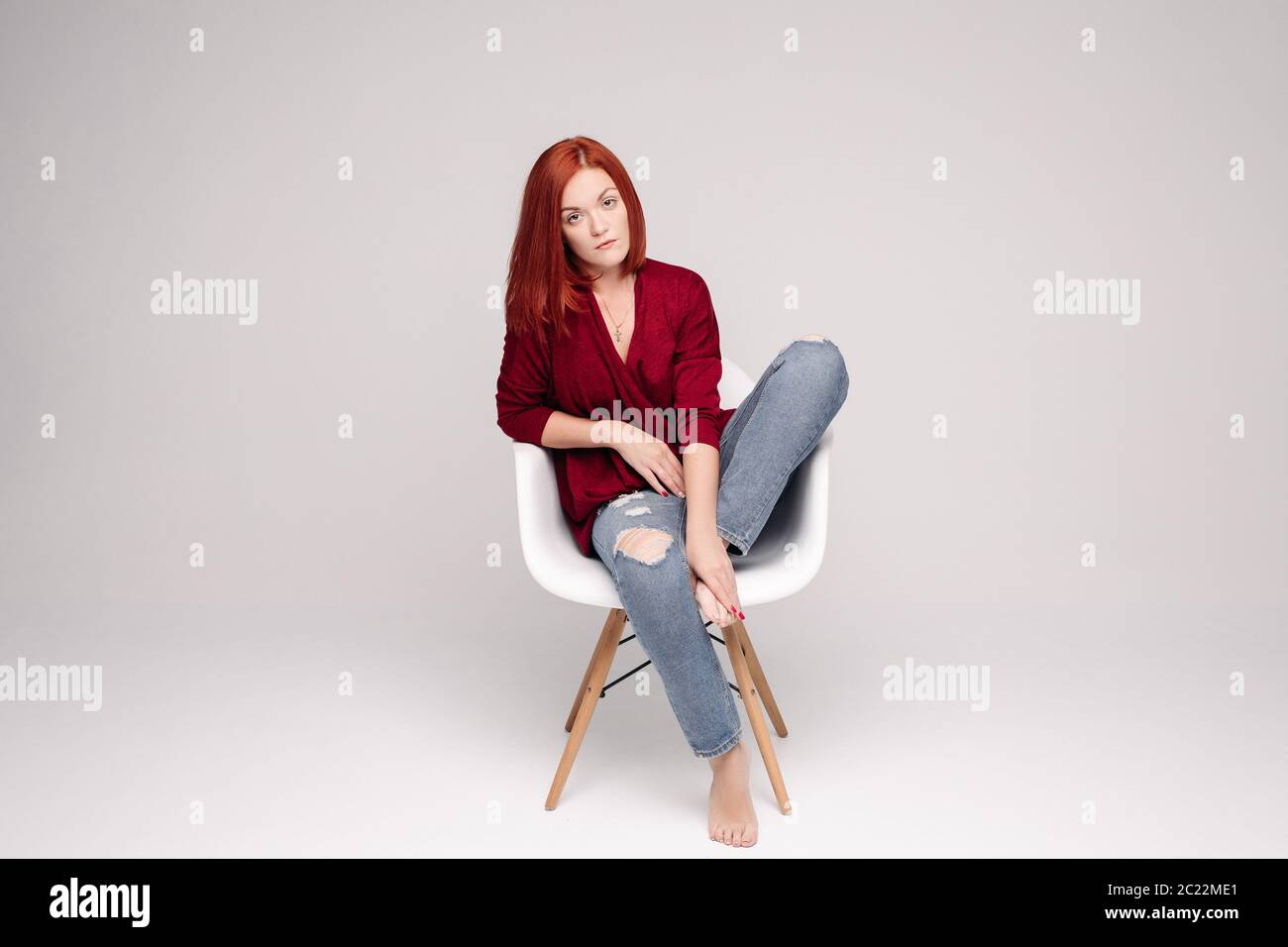 Model with ginger hair sitting on white chair in studio. Stock Photo