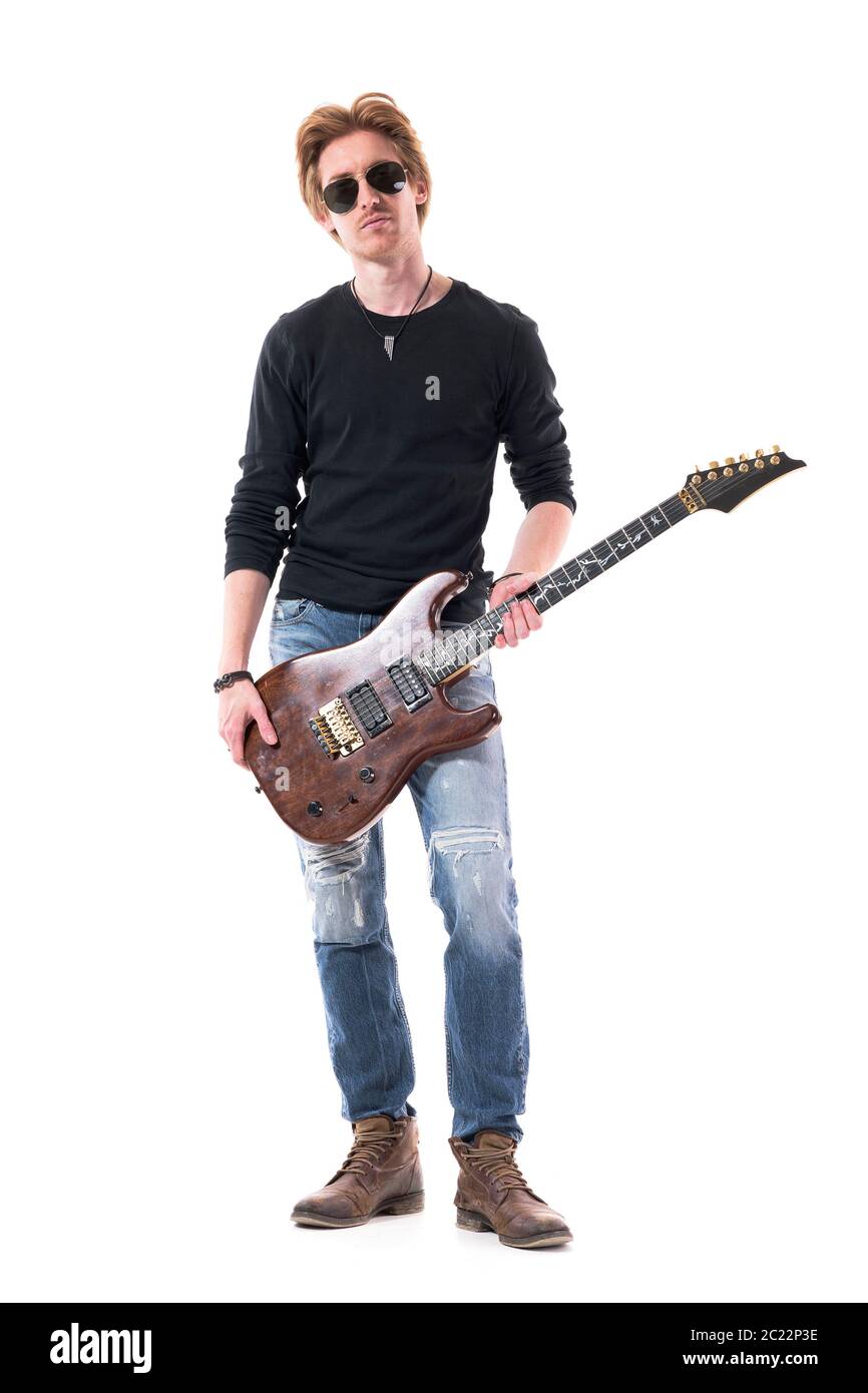 Cool attitude serious young rock musician male holding electric guitar looking at camera. Full body length isolated on white background. Stock Photo