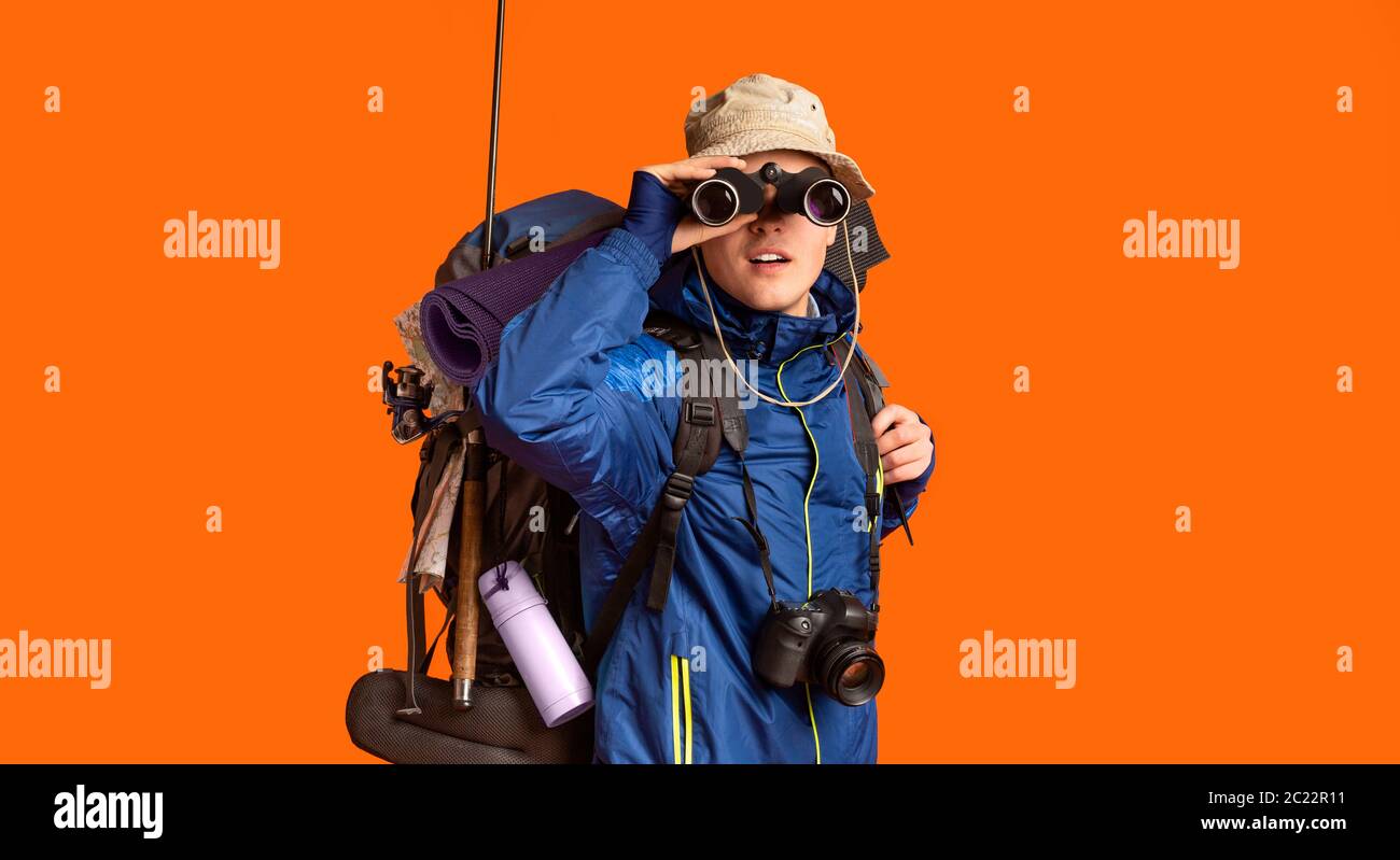 Excited backpacker looking towards camera through binoculars Stock Photo