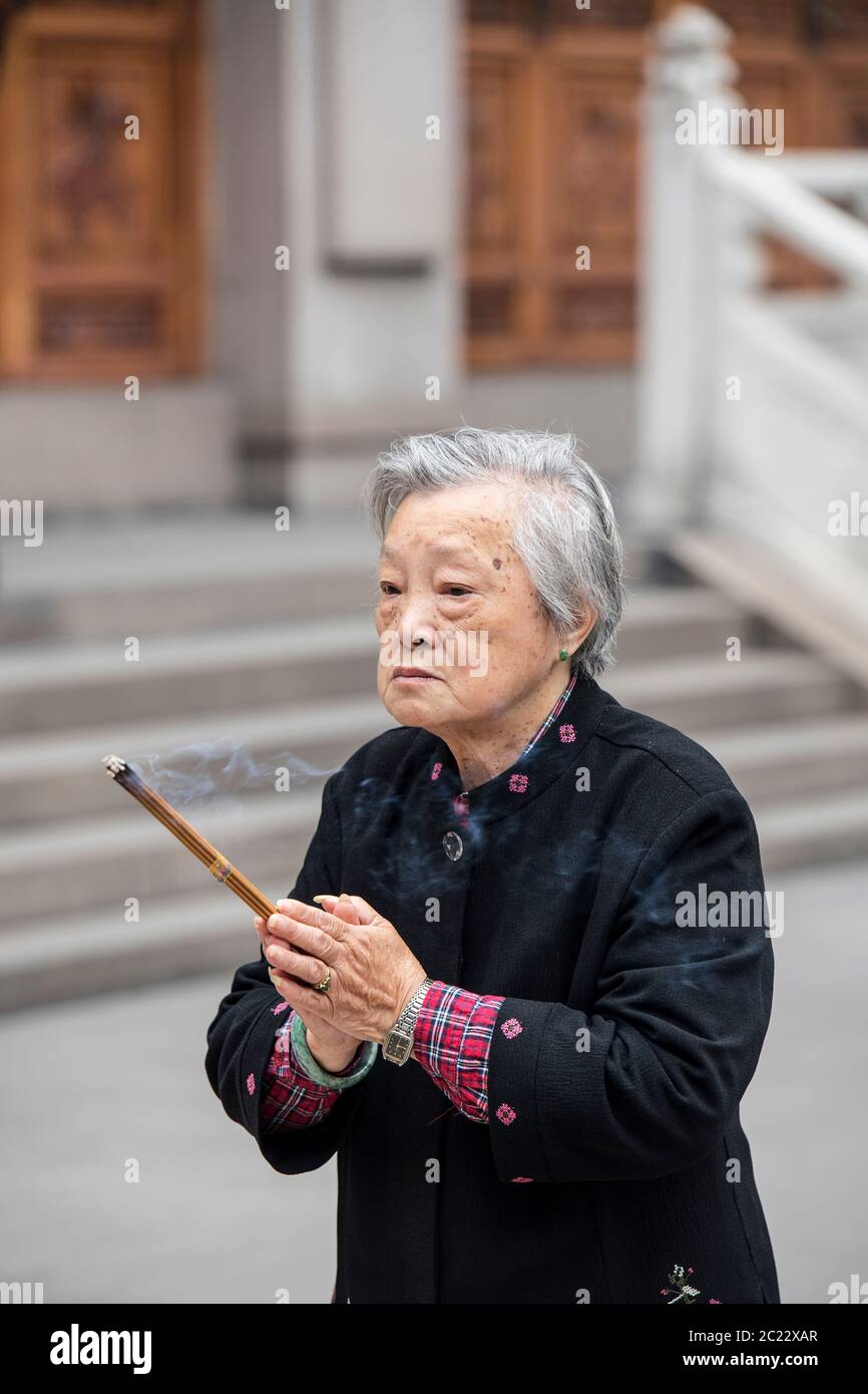 Elderly woman holding an incense stick at the Jing'an Temple in Shanghai, China Stock Photo