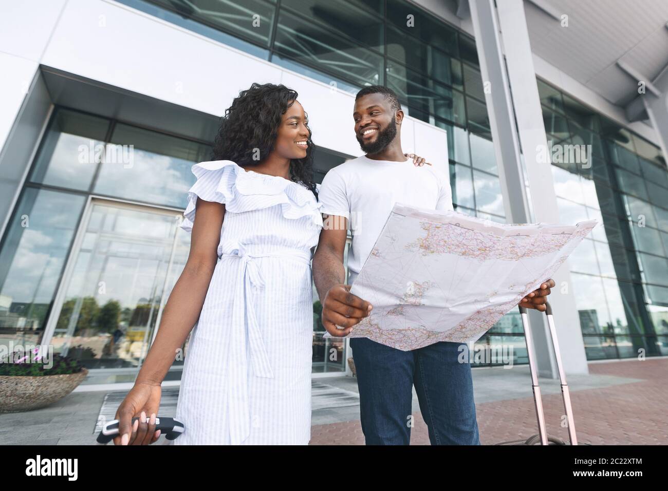 Happy african couple walking out of airport with map in hands Stock Photo