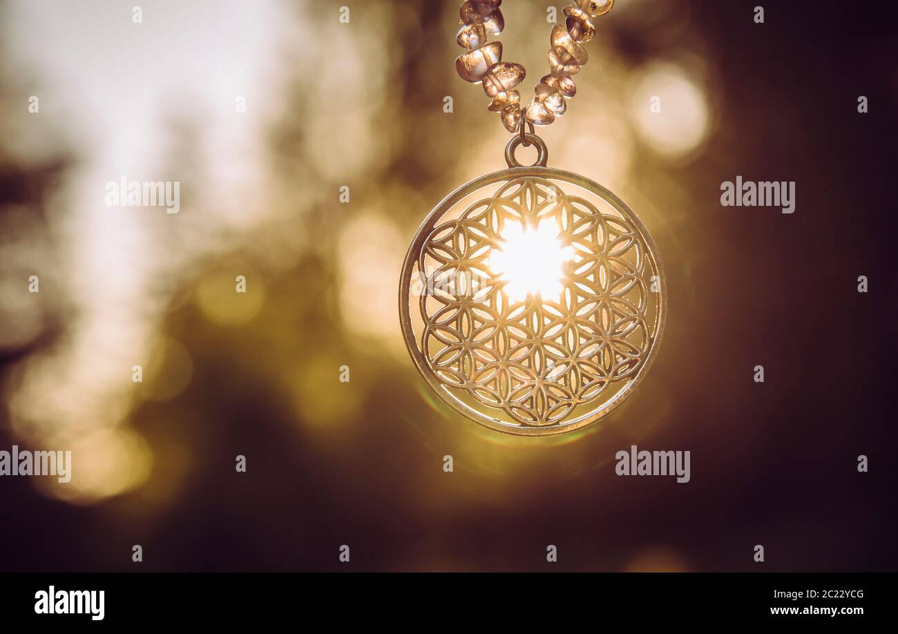 Flower of Life symbol pendant with sun shining though hanging outdoors with lot of copy space. Stock Photo