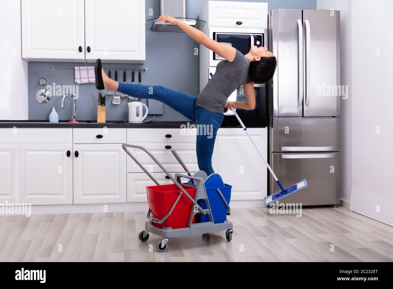 Close-up Of A Young Woman Slipping While Mopping Floor In The Kitchen Stock Photo