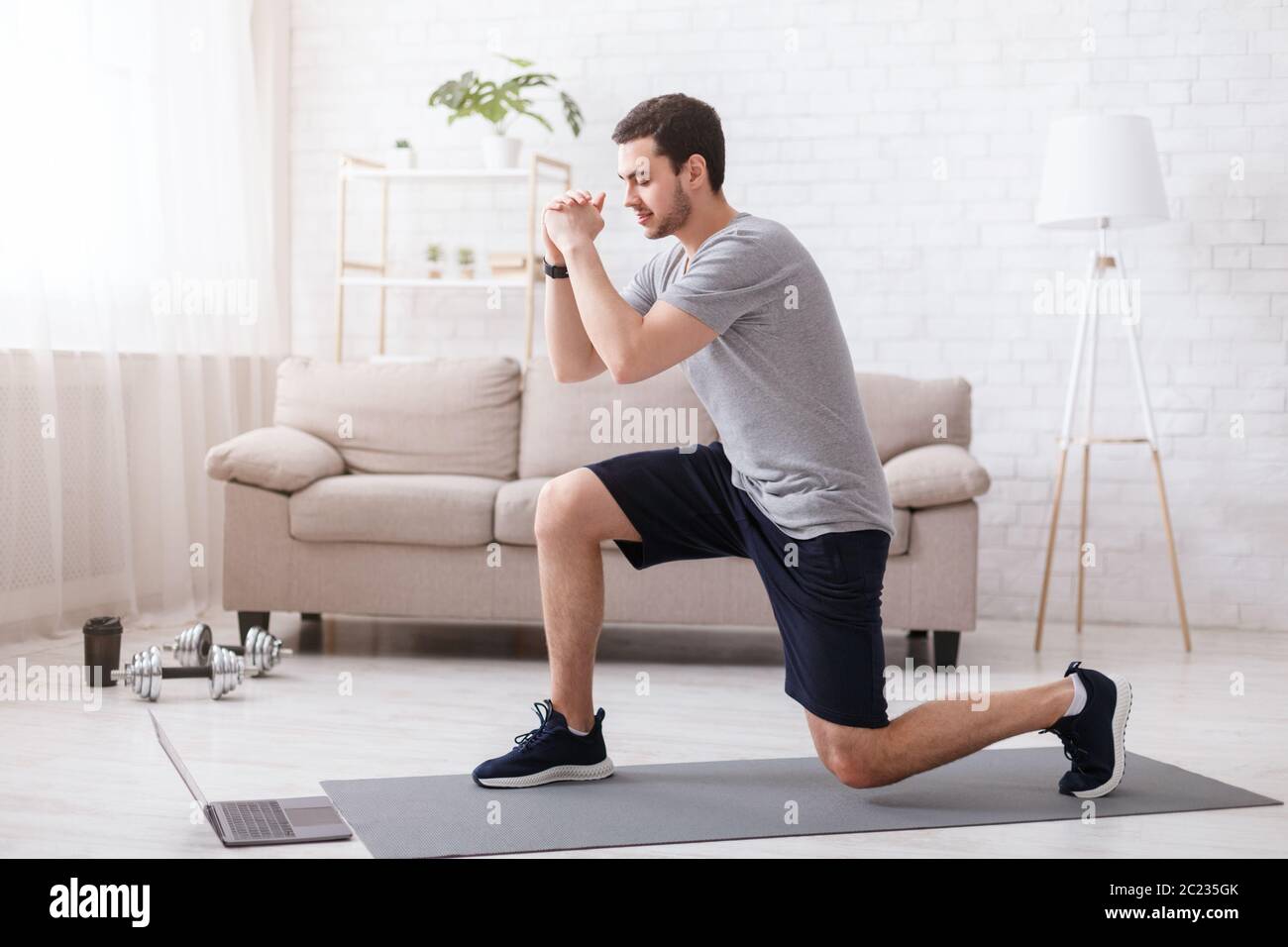 Sport activities at home. Young man watches online exercises and doing lunges Stock Photo