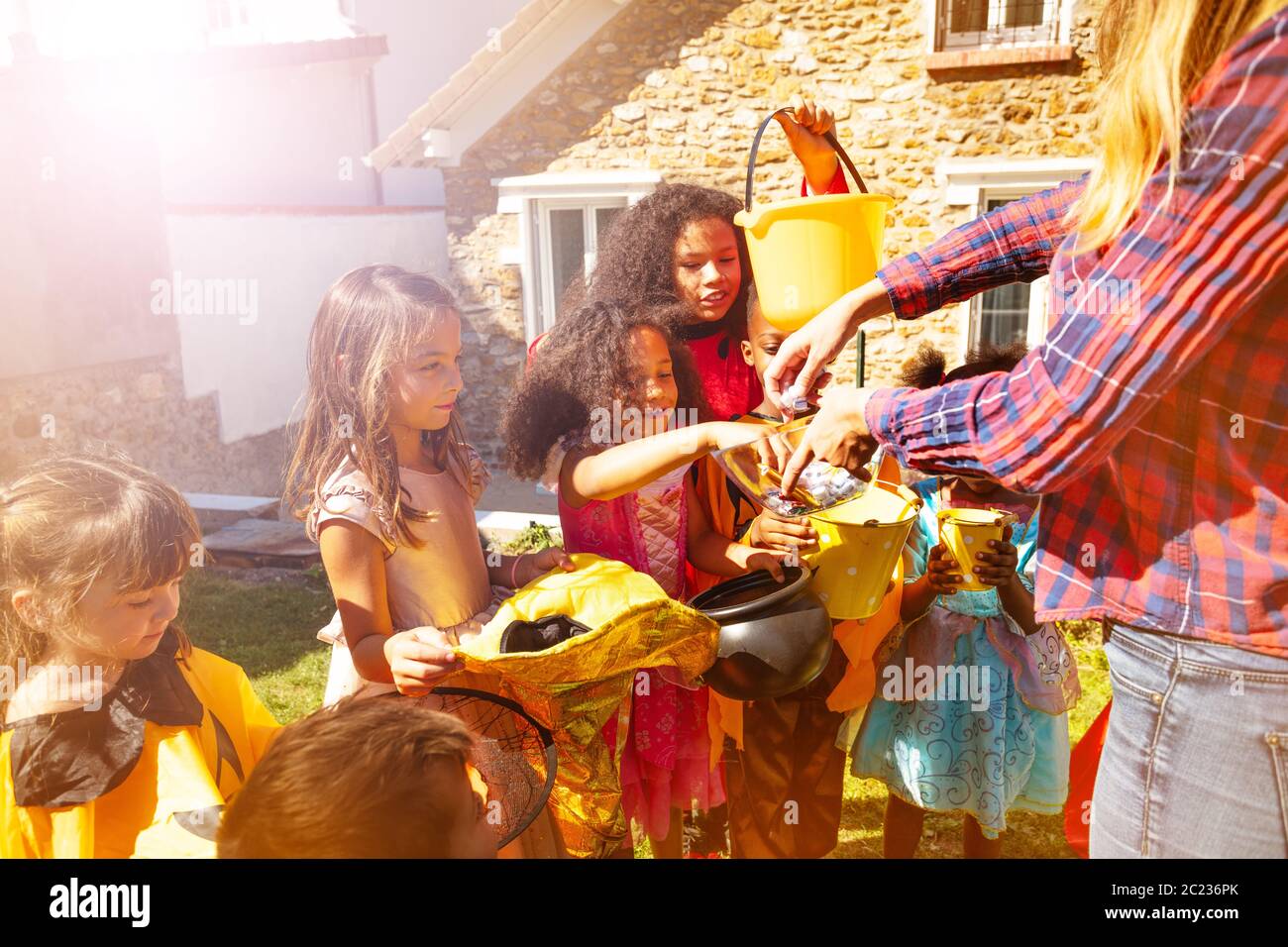 Group Of Kids On Halloween Wearing Cute Costumes Receive Candies From Adult On The Lawn In Front Of The House Stock Photo Alamy