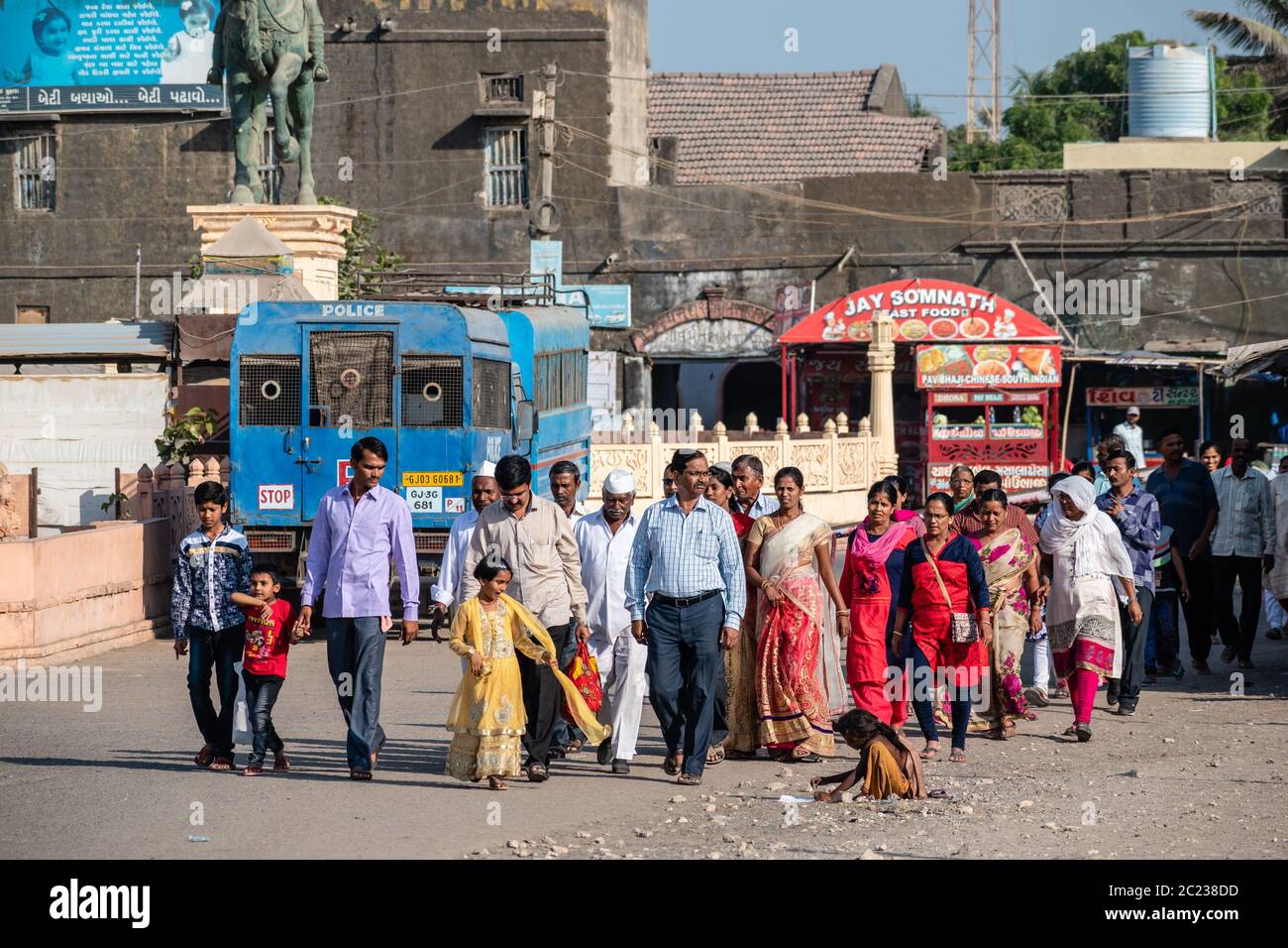 Somnath, Gujarat, India - December 2018:  A large group of Indian tourists walk past a poor girl begging on the street. Stock Photo