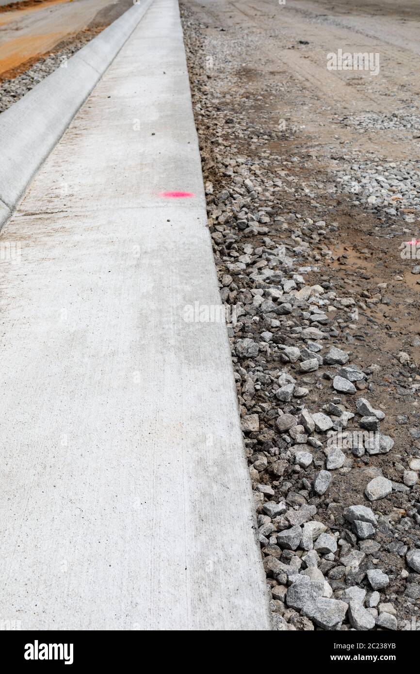 Long view down freshly extruded concrete curb beside road bed under