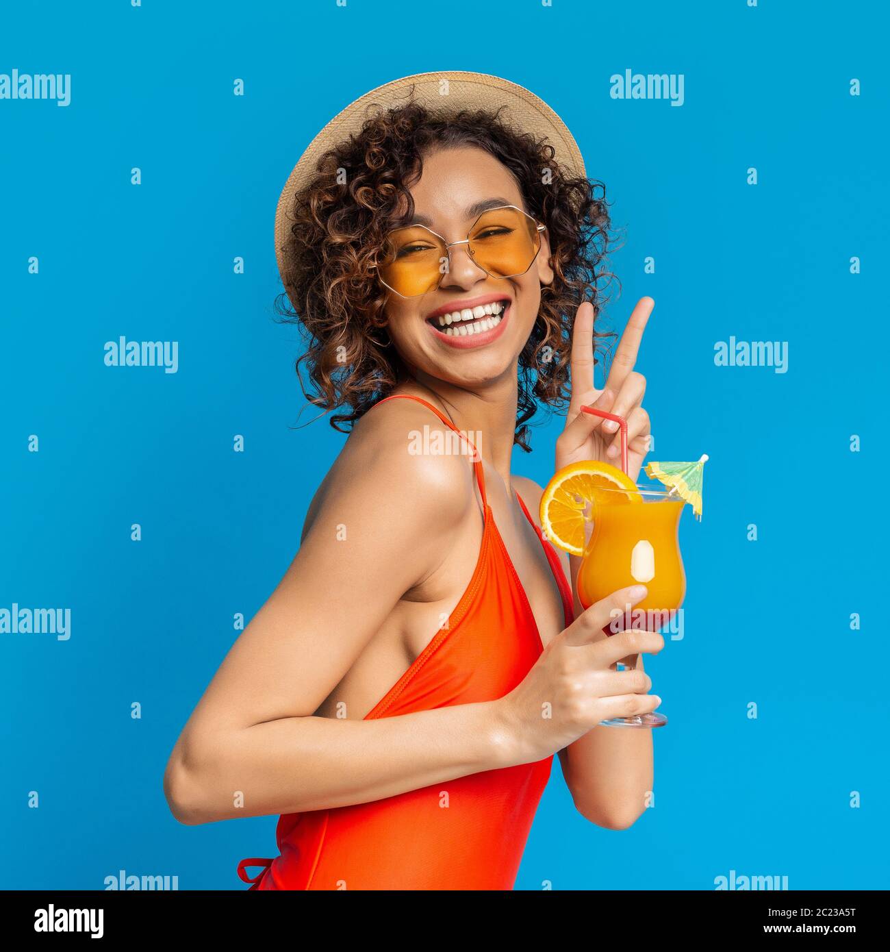 Joyful black girl in swimsuit enjoying summer cocktail and showing peace sign Stock Photo