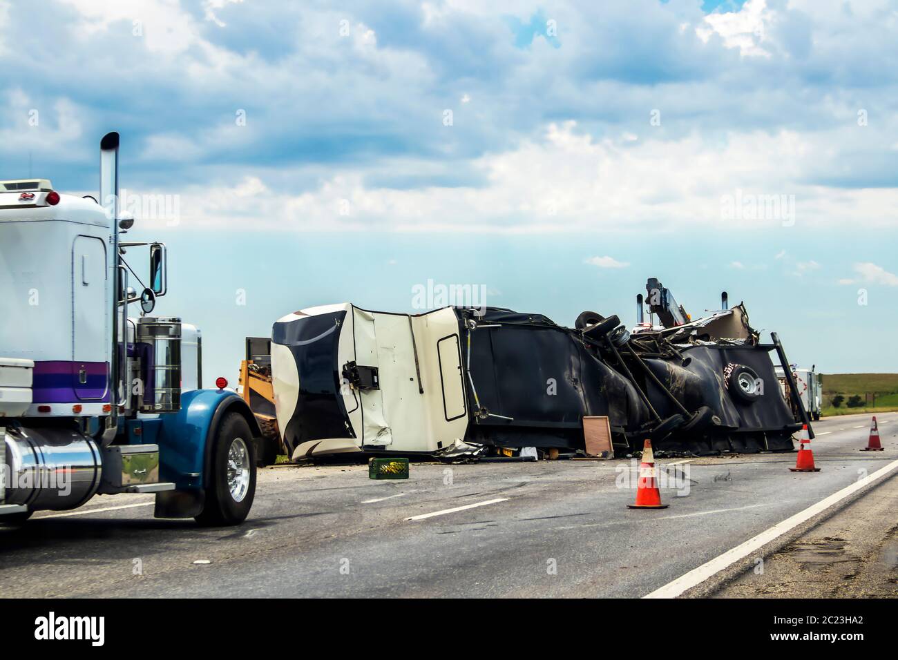 Fifth wheel RV overturned on highway with wench truck trying to get it off the road and two semis parked nearby and traffic cones keeping traffic away Stock Photo
