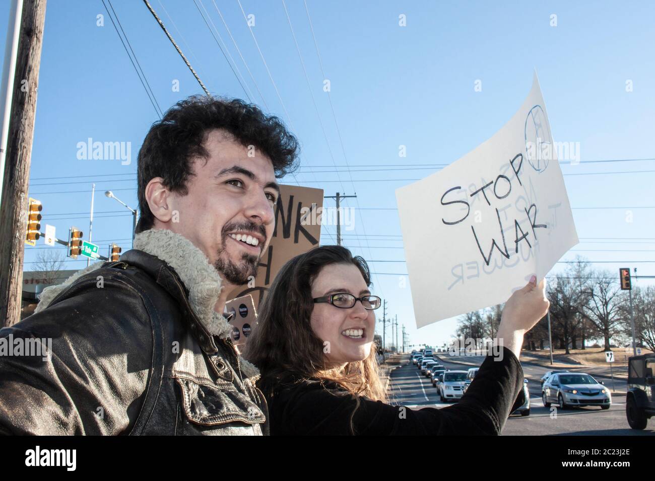 01-04-2010 Tulsa USA - Two smiling young people with a Stop War sign standing by city intersection with traffic Stock Photo