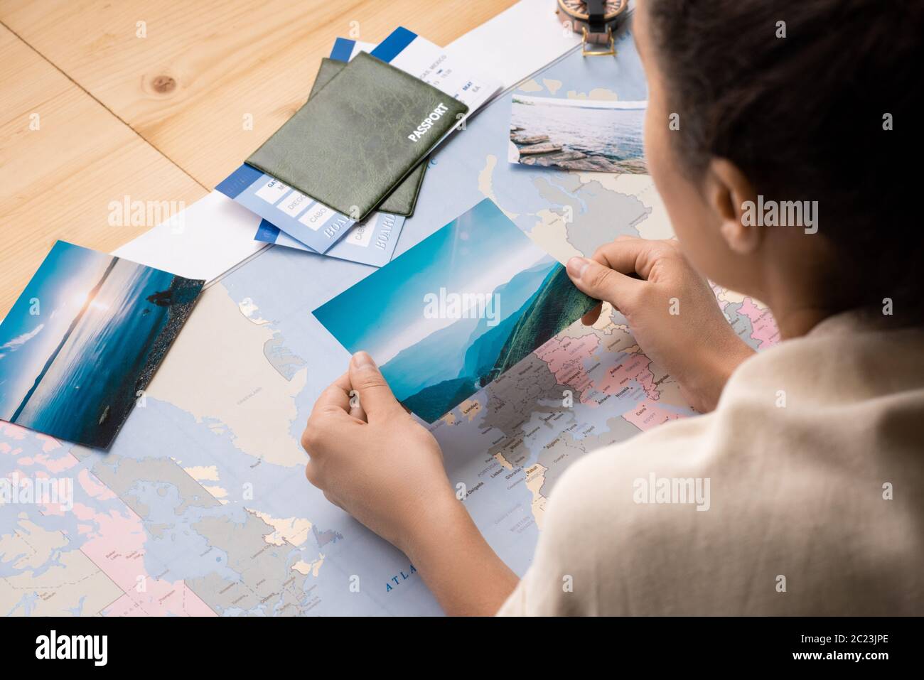 Over shoulder view of woman leaning on table with world map and watching photos while dreaming of travel Stock Photo