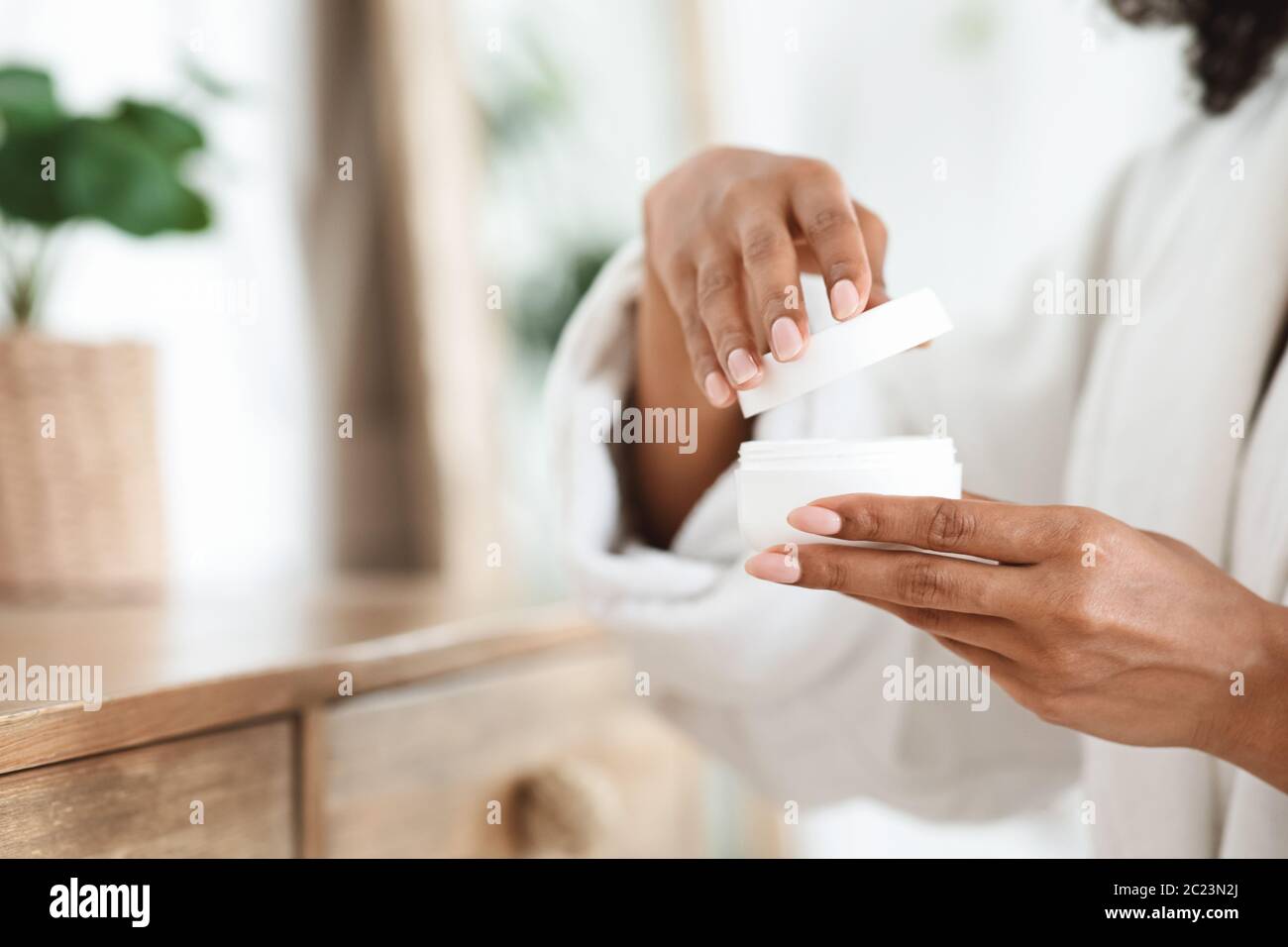 African woman opening jar of skin cream, ready for daily beauty routine Stock Photo