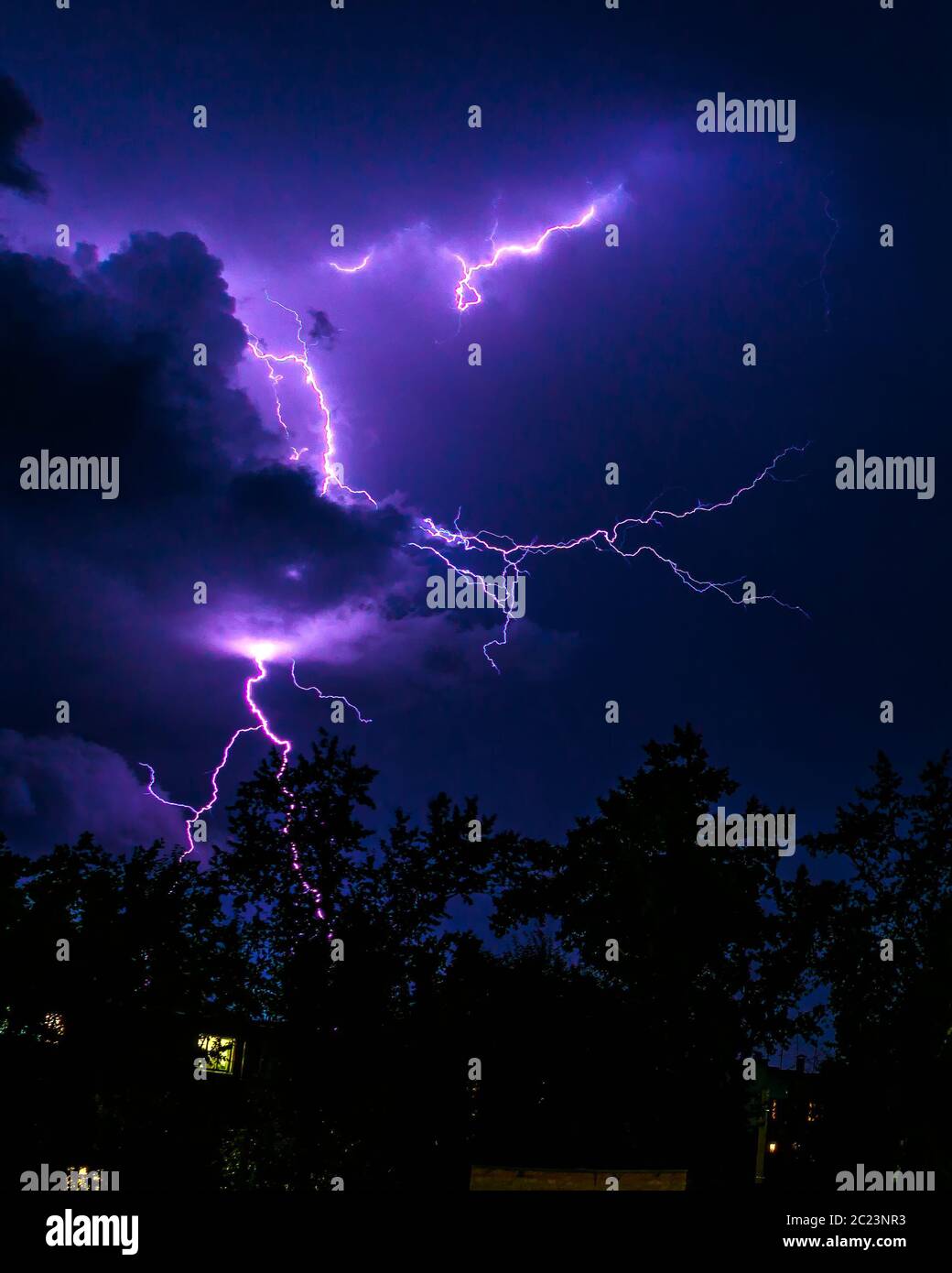 bright flashes of lightning during night thunderstorms, silhouettes of trees and houses against the dark blue sky Stock Photo