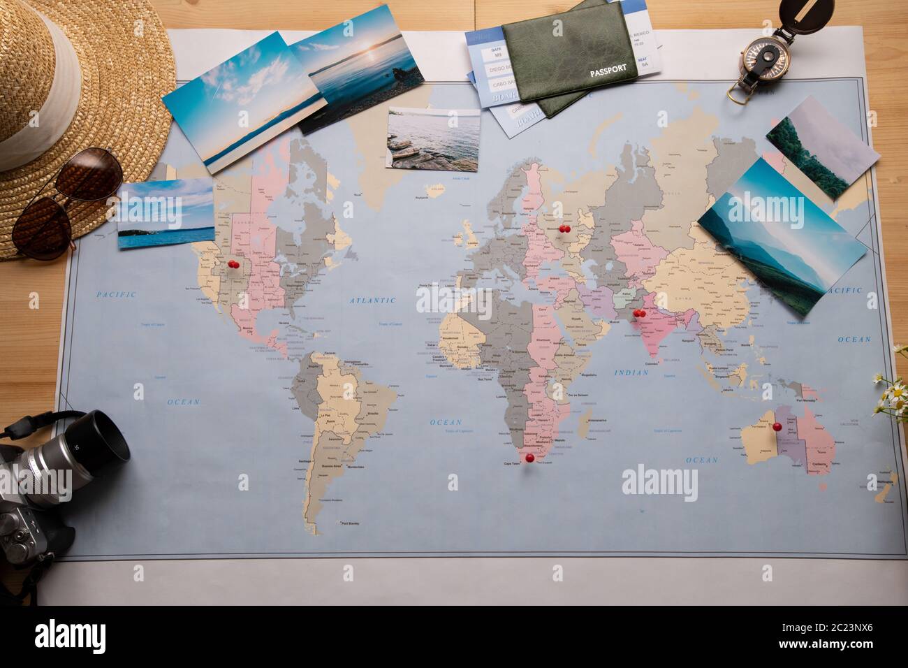 Above view of paper world map with red pins and beautiful nature photographs, camera, compass, sun hat and passports around Stock Photo