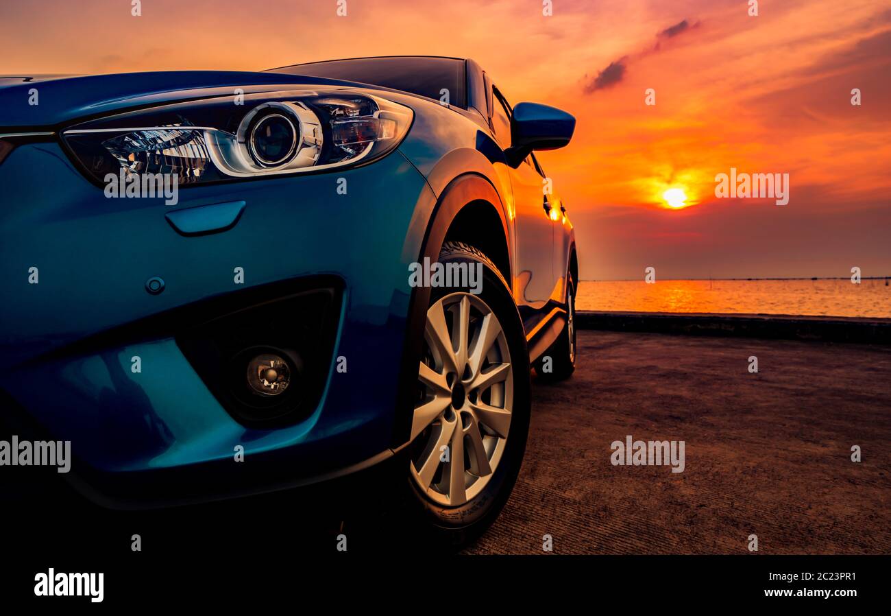 Blue compact SUV car with sport and modern design parked on concrete road by the sea at sunset. Environmentally friendly technology. Business success concept. Stock Photo