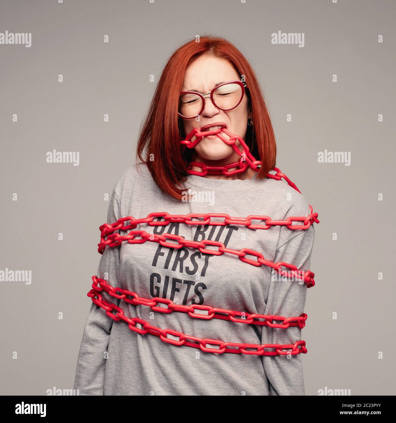 girl entangled in a chain,A red-haired woman with brown hair tries to get rid of the chain Stock Photo