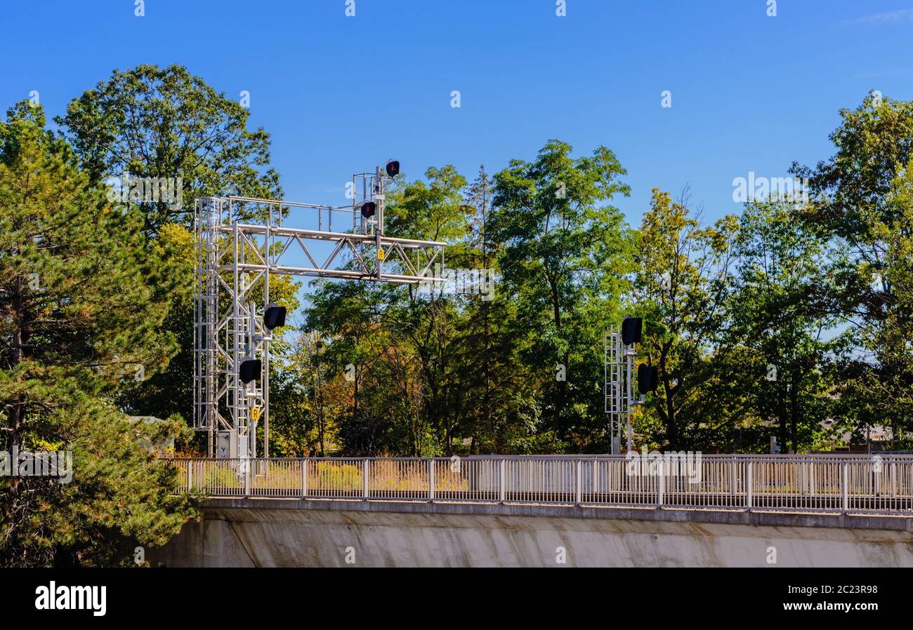 Railway signals and signs on metal frame above bridge with fence among trees. Stock Photo