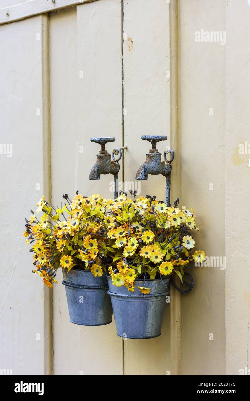 Bucket with flowers hanging on an aged faucet Stock Photo