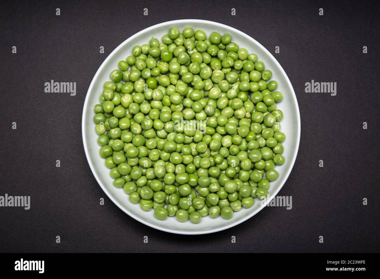 Top view of a plate with fresh Green pea isolated on black background. Pisum sativum Stock Photo
