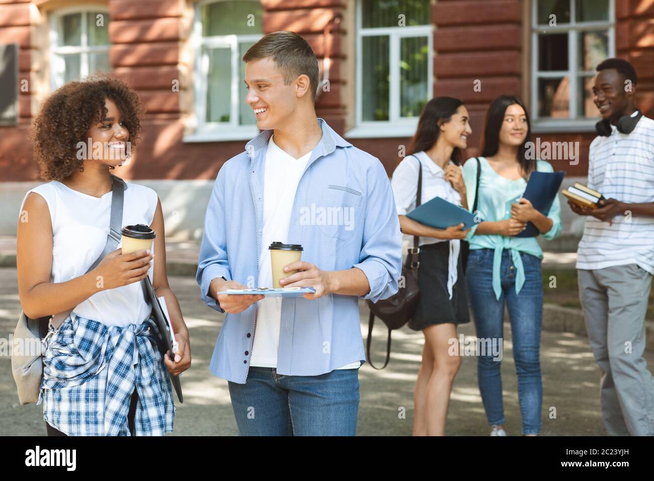 Joyful Multi-Ethnic Students Drinking Coffee At Campus Courtyard, Resting Between Classes Stock Photo