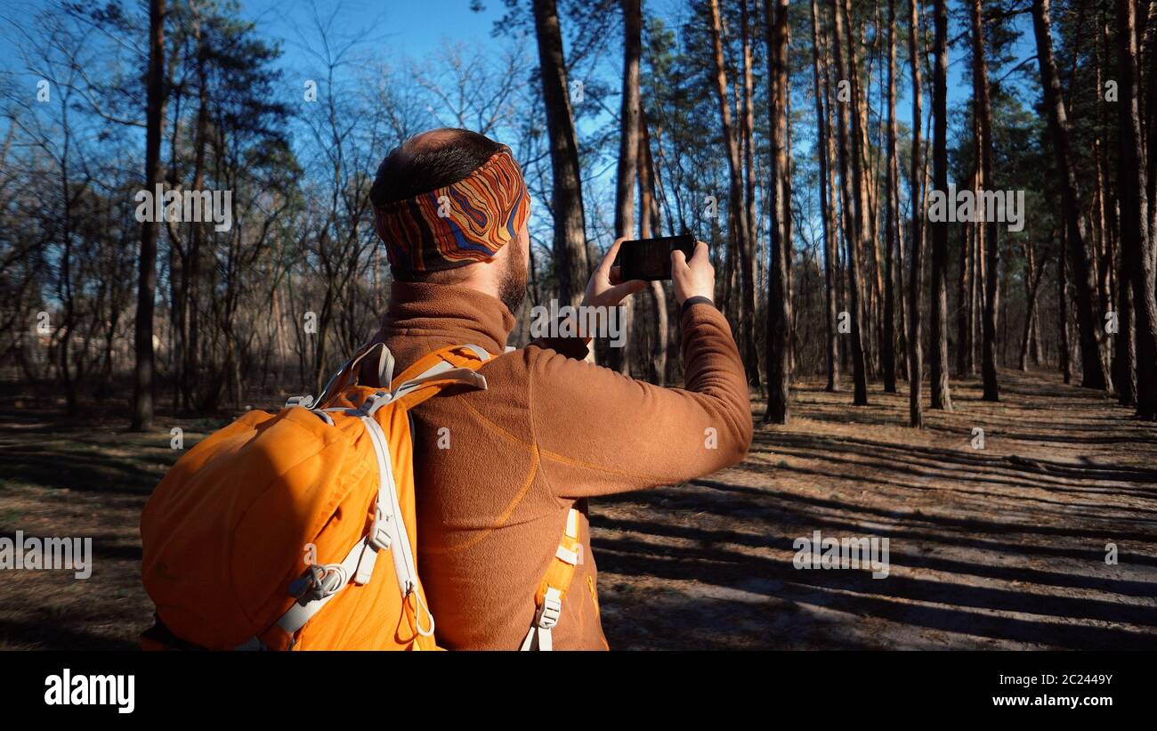 theme tourism hiking forest and technology. Man Caucasian male beard traveler uses hand phone make photo video with backpack act Stock Photo