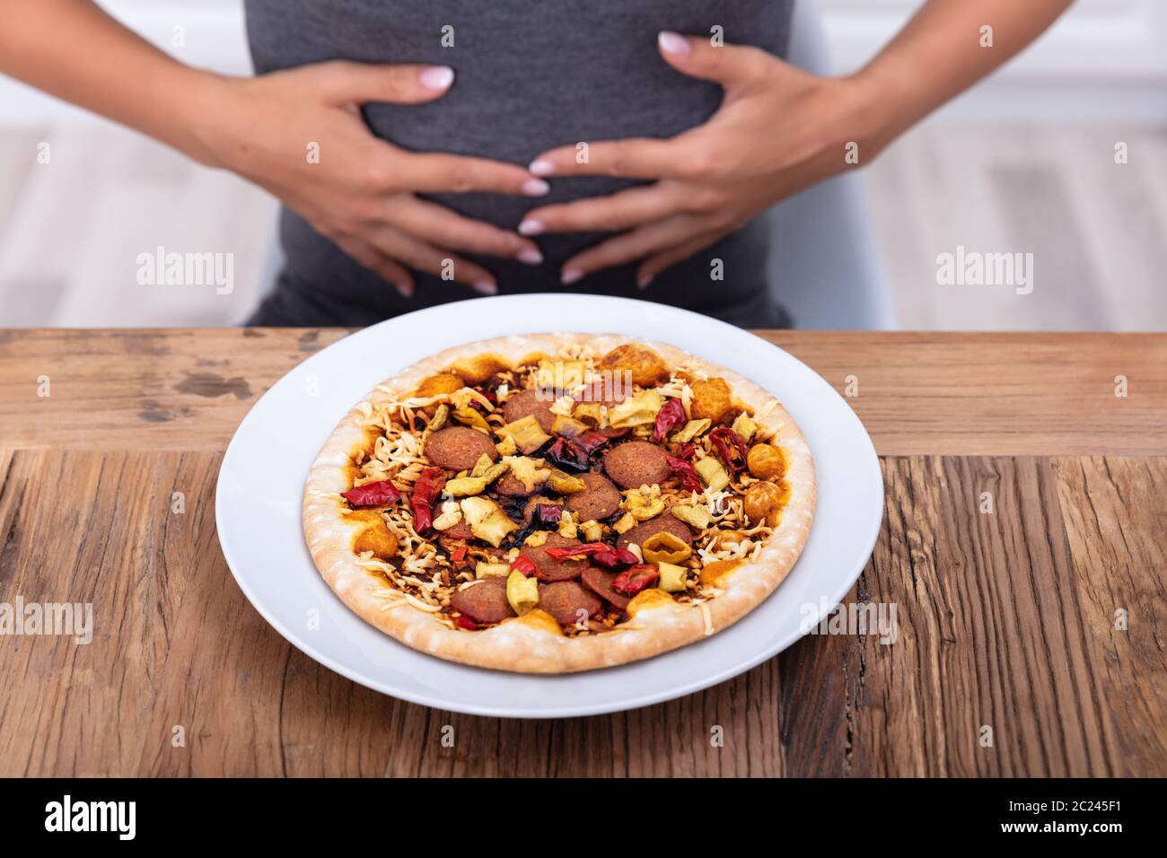 Young Woman Suffering From Stomach Pain While Having Pizza Stock Photo