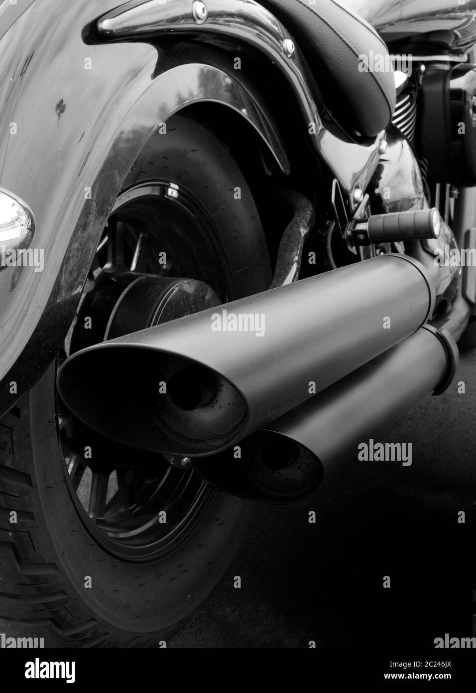 monochrome close up of the back of a vintage motorcycle with rear wheel mudguard and wide exhaust pipes Stock Photo