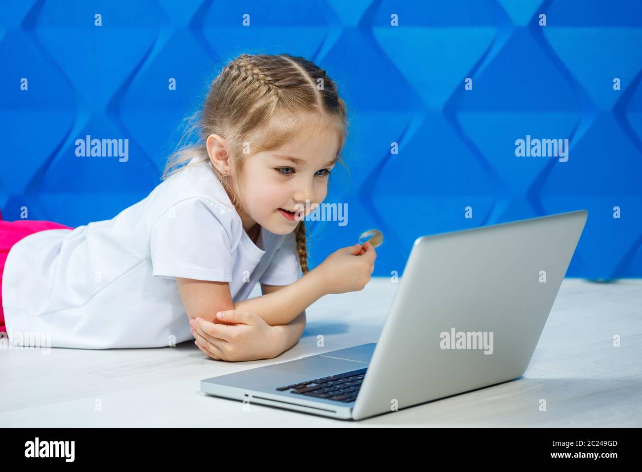 A modern child girl uses a laptop lying on the floor with legs looking ...