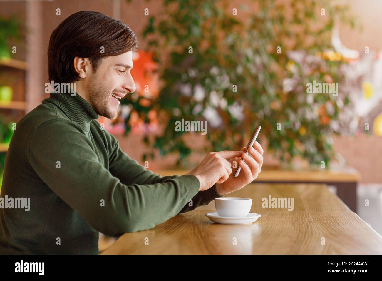 Young man using smartphone while drinking coffee at cafe Stock Photo
